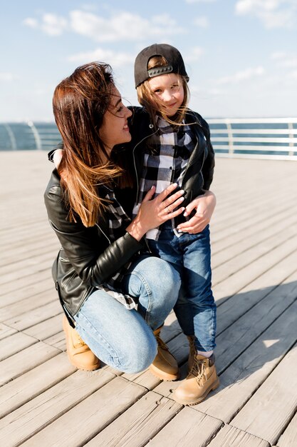 Retrato de cuerpo entero de una mujer bonita con una pequeña hija vistiendo trajes similares posando al aire libre en la luz del sol