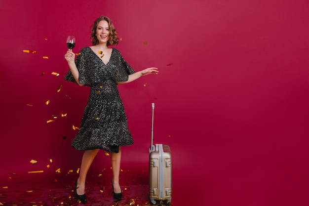 Retrato de cuerpo entero de una mujer elegante y bien formada bailando con un vaso de bebida alcohólica