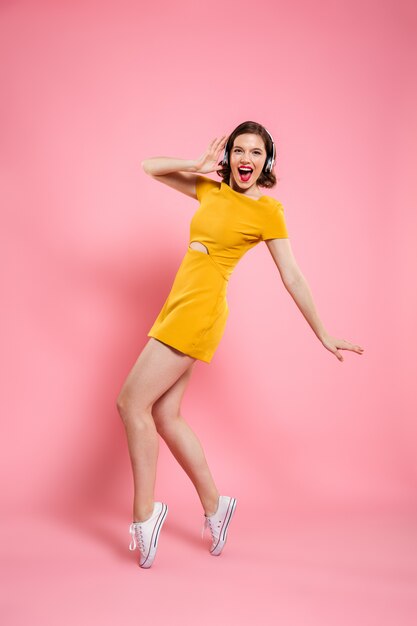 Retrato de cuerpo entero de una mujer encantadora feliz en auriculares de pie sobre los pies