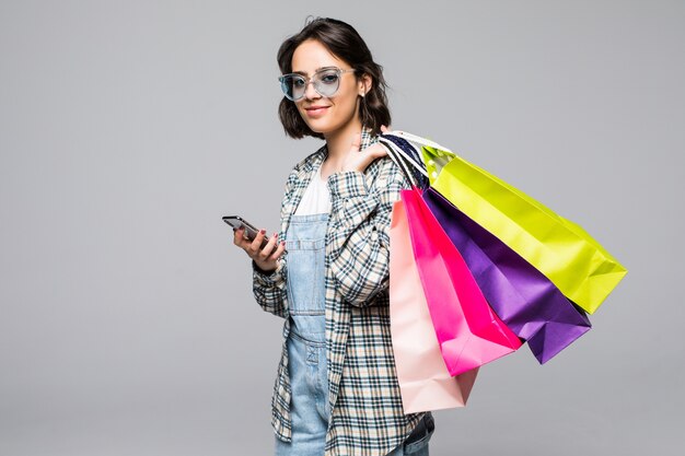 Retrato de cuerpo entero de una mujer joven feliz con bolsas de la compra y teléfono móvil aislado