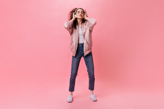 Foto gratuita retrato de cuerpo entero de mujer rizada en jeans bailando mientras escucha música en auriculares