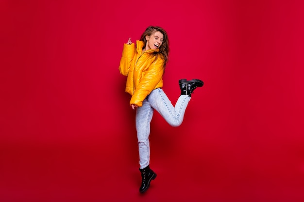 Foto gratuita retrato de cuerpo entero de una niña feliz activa con pelo largo vestida de amarillo jacker y jeans con sonrisa feliz sobre la pared roja. retrato de una mujer joven frustrada en vestido aislado sobre fondo rojo.