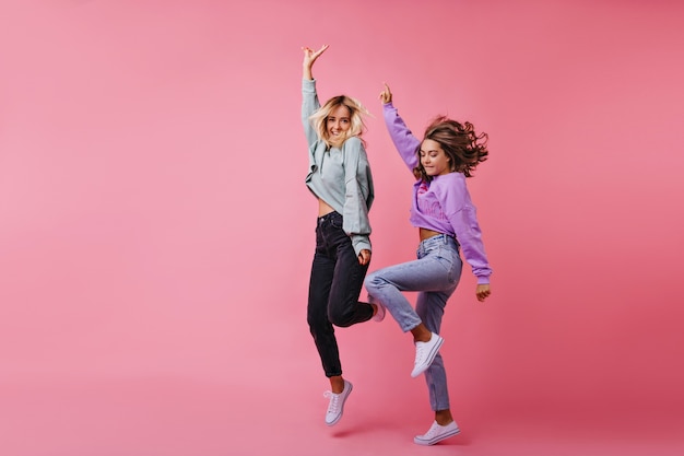 Retrato de cuerpo entero de niñas blancas saltando expresando emociones felices. Retrato de mejores amigos divertidos bailando juntos.