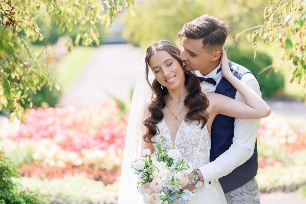 Retrato de cultivo de novio guapo en traje besando a la novia bonita desde atrás posando juntos en el jardín Disfrutando de un momento tierno el día de la boda Hermosa novia con maquillaje de boda natural