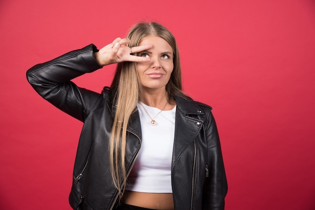 Retrato de dama adorable que muestra el signo v cerca del ojo aislado sobre una pared roja