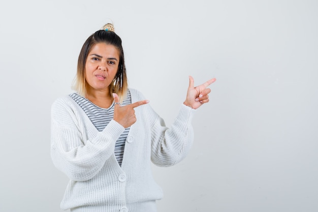 Retrato de dama encantadora apuntando a la esquina superior derecha en camiseta, cárdigan y aspecto sensato