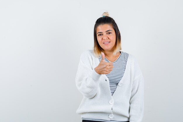 Retrato de dama encantadora mostrando el pulgar hacia arriba en camiseta, cárdigan y mirando alegre vista frontal