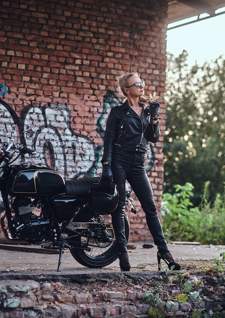 Retrato de una dama madura y atractiva junto a su moto vintage y pared de ladrillos de graffiti.