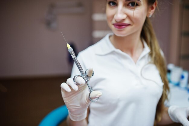 Retrato de una dentista con bata blanca posando con una jeringa llena de anestesia en un gabinete dental