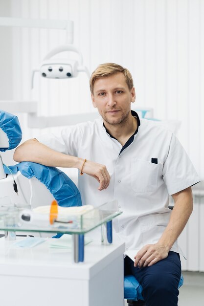 Retrato del dentista sonriente del hombre caucásico que presenta en el consultorio dental moderno.