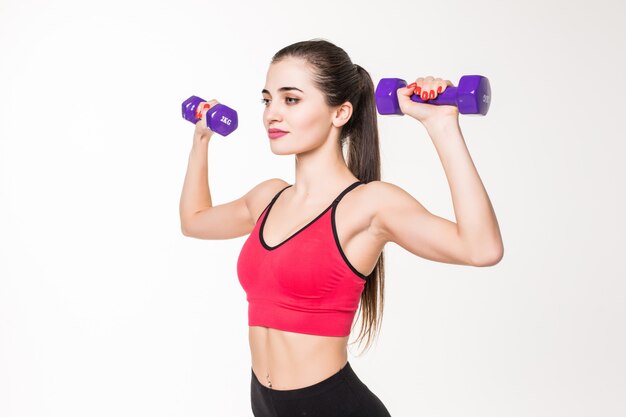 Retrato de una deportista bastante joven haciendo ejercicios con pesas aislado en una pared blanca