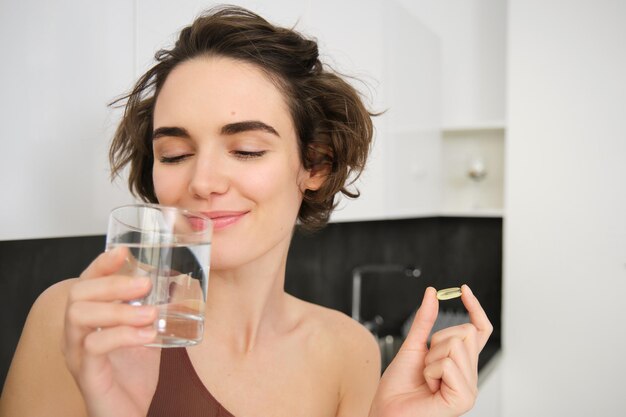 Retrato de deportista bebiendo agua tomando suplementos dietéticos de vitaminas para una piel sana con om