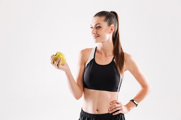 Retrato de una deportista bonita sana que sostiene la manzana verde