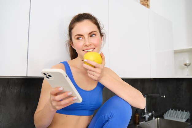 Retrato de una deportista comiendo una manzana y mirando la pantalla de su teléfono inteligente de redes sociales