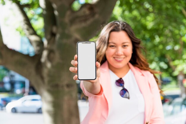 Retrato desenfocado de una mujer joven que muestra la pantalla de visualización en blanco del teléfono móvil