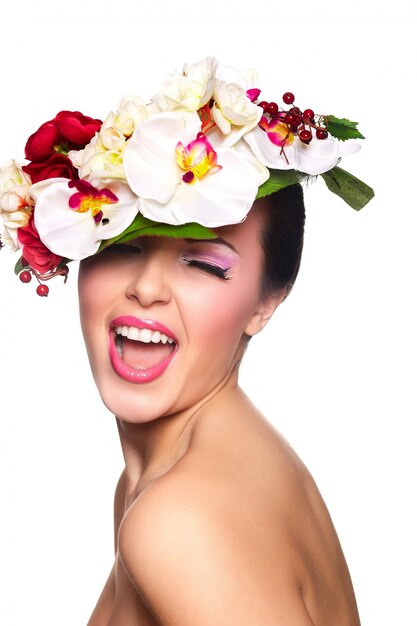 Retrato de detalle de la hermosa modelo de morena caucásica sonriente joven sexy con labios glamour, maquillaje brillante. Con flores de colores en la cabeza