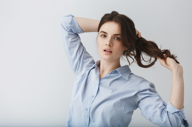 Retrato dinámico de la hermosa joven morena desenlazando su cabello con las manos con expresión relajada.