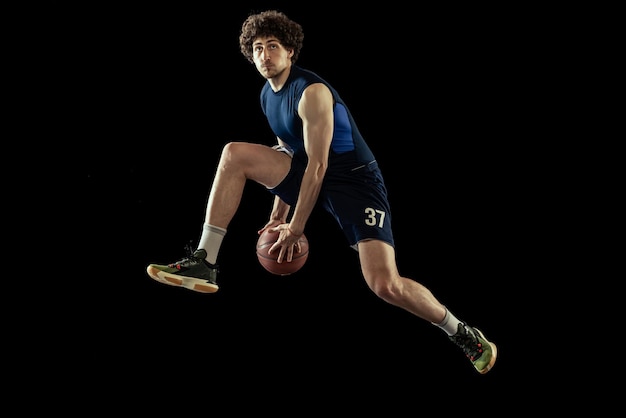 Foto gratuita retrato dinámico de un joven jugando al baloncesto de entrenamiento aislado sobre fondo negro de estudio