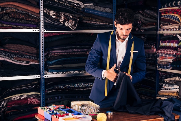 Retrato de un diseñador de moda masculino cortando la tela con tijera en su taller