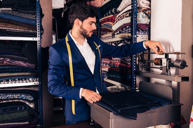 Retrato de un diseñador de moda masculino que ajusta la máquina de báscula de pesaje de tela en el taller