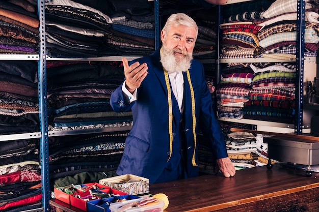 Retrato de un diseñador de moda masculino senior invitando a alguien en su tienda