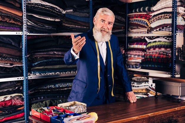 Retrato de un diseñador de moda masculino senior invitando a alguien en su tienda