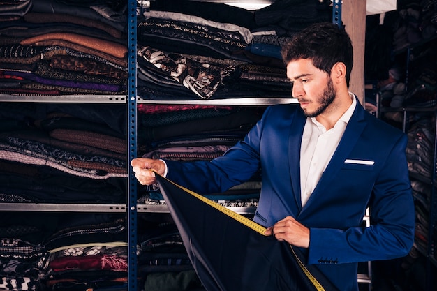 Retrato de un diseñador de moda tomando medidas de tela en su tienda