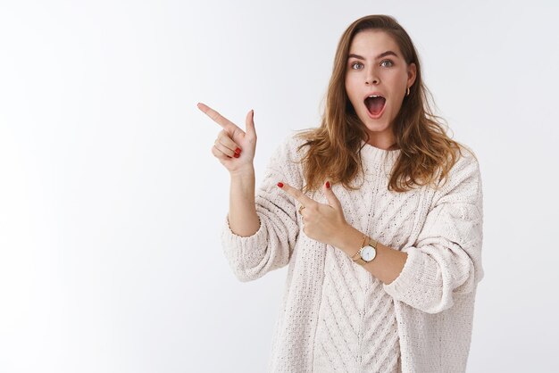 Retrato divertido asombrado mudo modelo femenino vistiendo suéter caída mandíbula impresionado apuntando hacia los lados