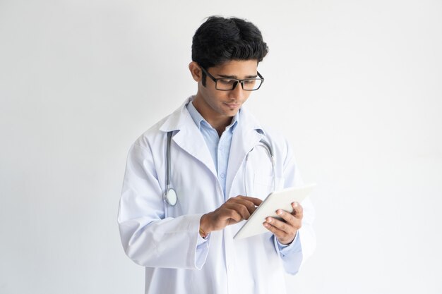 Retrato del doctor confidente joven en vidrios usando la tableta de la PC.