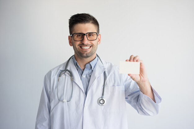 Retrato del doctor joven sonriente que muestra la tarjeta de visita.