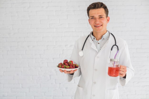 Retrato del doctor de sexo masculino que sostiene las frutas y el smoothie de la fresa