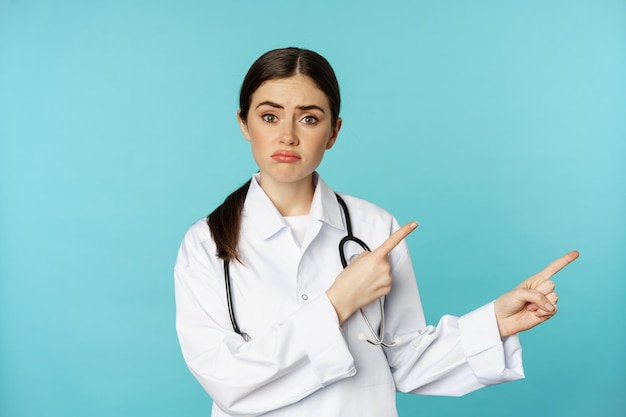 Retrato de una doctora decepcionada trabajadora médica señalando con el dedo a la derecha y mirando triste arrepentimiento g...