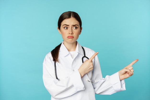 Foto gratuita retrato de una doctora decepcionada trabajadora médica señalando con el dedo a la derecha y mirando triste arrepentimiento g...