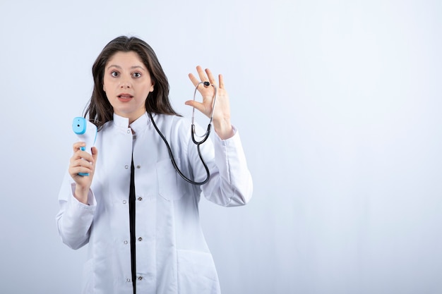 Retrato de doctora mostrando termómetro y estetoscopio en gris.