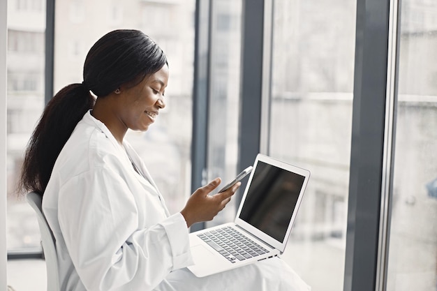 Retrato de una doctora negra sentada en su oficina en la clínica y usando una laptop