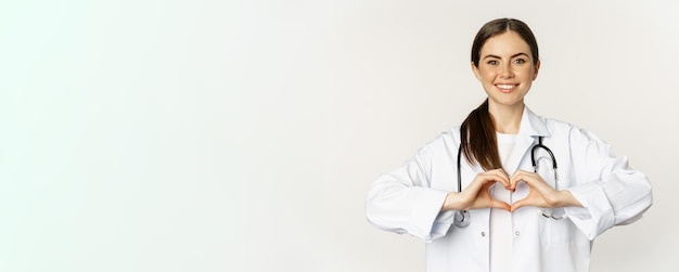 Retrato de una doctora sonriente que muestra el signo del corazón y mira con cuidado ama a su paciente