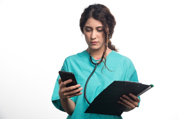 Retrato de doctora sosteniendo un teléfono móvil con portapapeles sobre fondo blanco. Foto de alta calidad