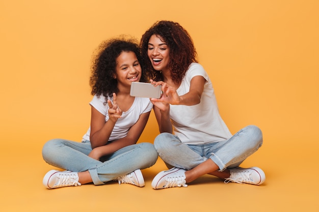 Retrato de dos hermanas afroamericanas alegres tomando selfie con smartphone