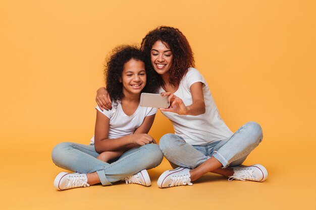 Retrato de dos hermanas afroamericanas alegres tomando selfie con smartphone