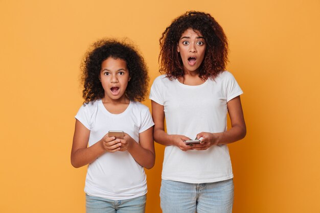 Retrato de dos hermanas afroamericanas sorprendidas con teléfonos inteligentes