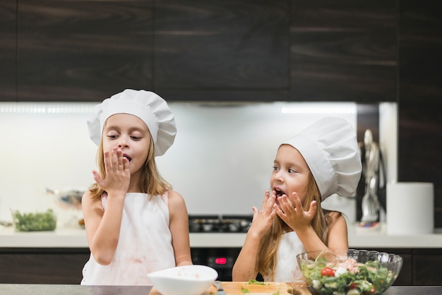 Retrato de dos hermanas que se lamen las manos mientras preparan la comida.