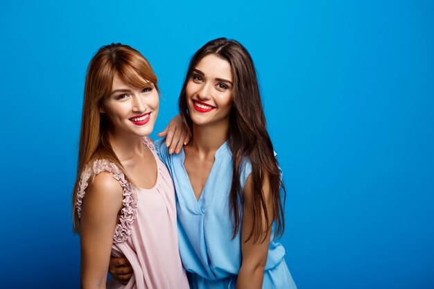 Retrato de dos hermosas chicas sobre pared azul