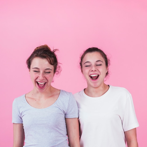 Foto gratuita retrato de dos jóvenes amigas riendo contra el fondo rosa