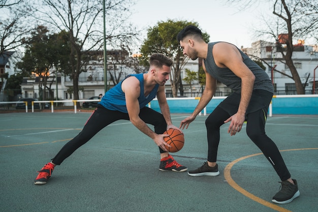 Retrato de dos jóvenes amigos jugando baloncesto y divirtiéndose en la cancha al aire libre. Concepto deportivo.