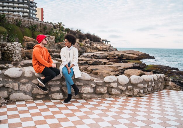 Retrato de dos jóvenes amigos que pasan un buen rato juntos y conversan mientras están sentados con el mar en el espacio.