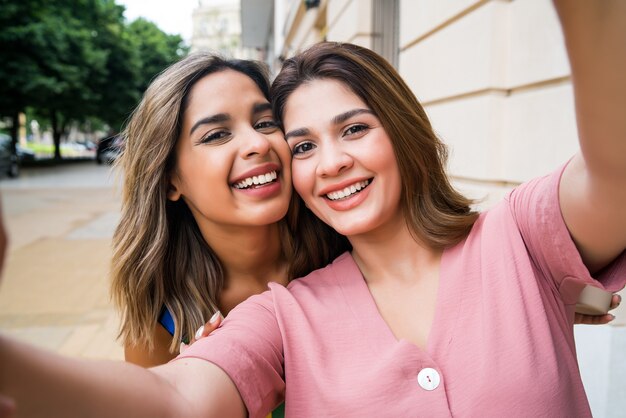 Retrato de dos jóvenes amigos tomando un selfie mientras está parado al aire libre en la calle