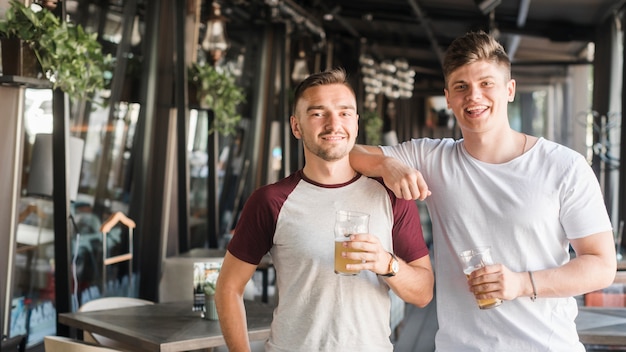 Foto gratuita retrato de dos jóvenes amigos varones con vasos de cerveza