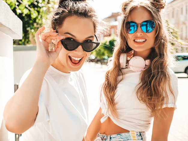 Retrato de dos jóvenes hermosas mujeres hipster sonrientes en ropa de camiseta blanca de verano de moda