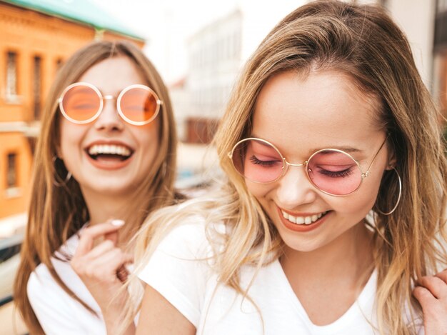 Retrato de dos jóvenes hermosas rubias sonrientes chicas hipster en ropa de moda verano camiseta blanca. . Modelos positivos divirtiéndose en gafas de sol.