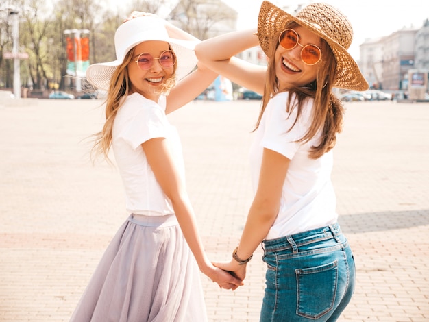 Foto gratuita retrato de dos jóvenes hermosas rubias sonrientes chicas hipster en ropa de moda verano camiseta blanca. . modelos positivos tomados de la mano